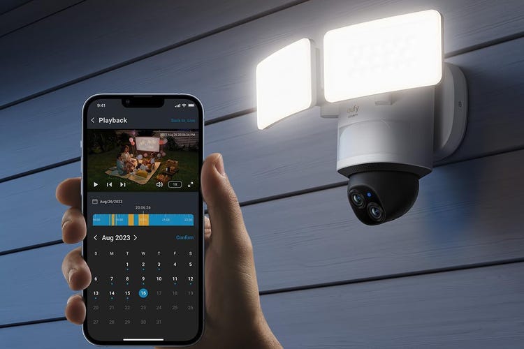 A phone app held up next to a Eufy floodlight camera on siding.
