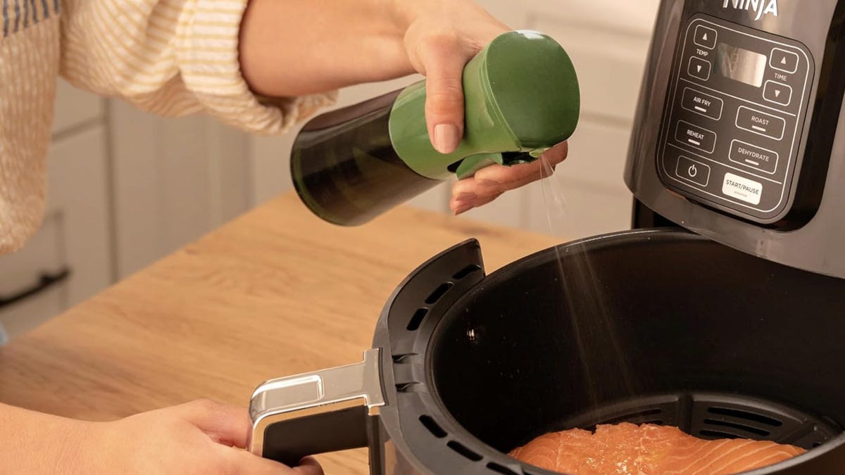 A person spraying salmon with oil in an air fryer basket.