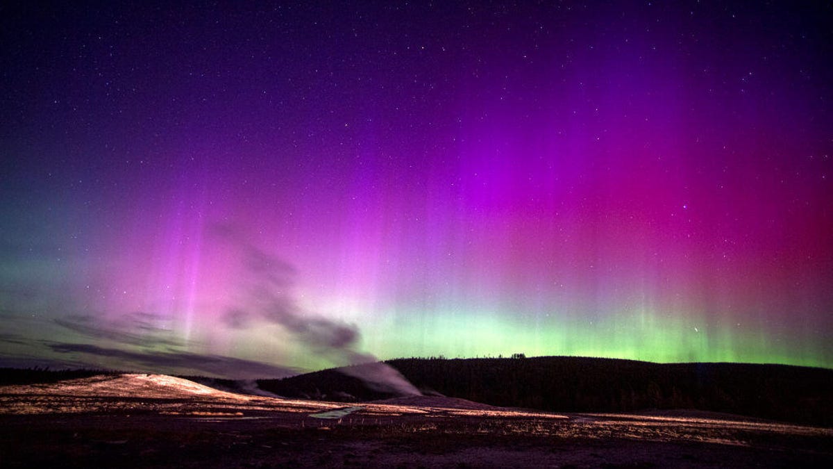 The aurora borealis turns the sky into a rainbow as the Old Faithful geyser steams.