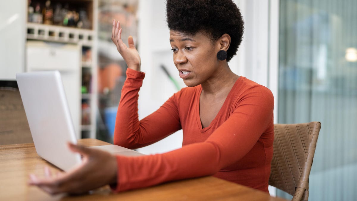 A woman shows frustration as she stares at her laptop with her hands raised.