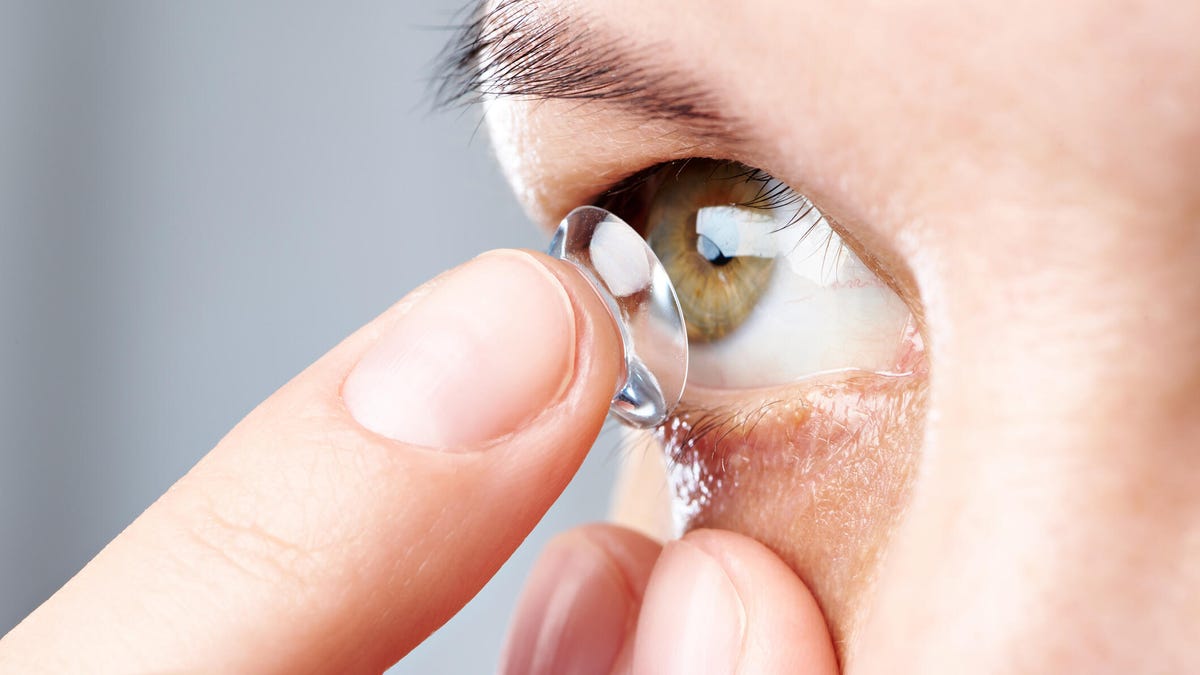 A close-up image of a person with a brown iris putting in a contact lens.