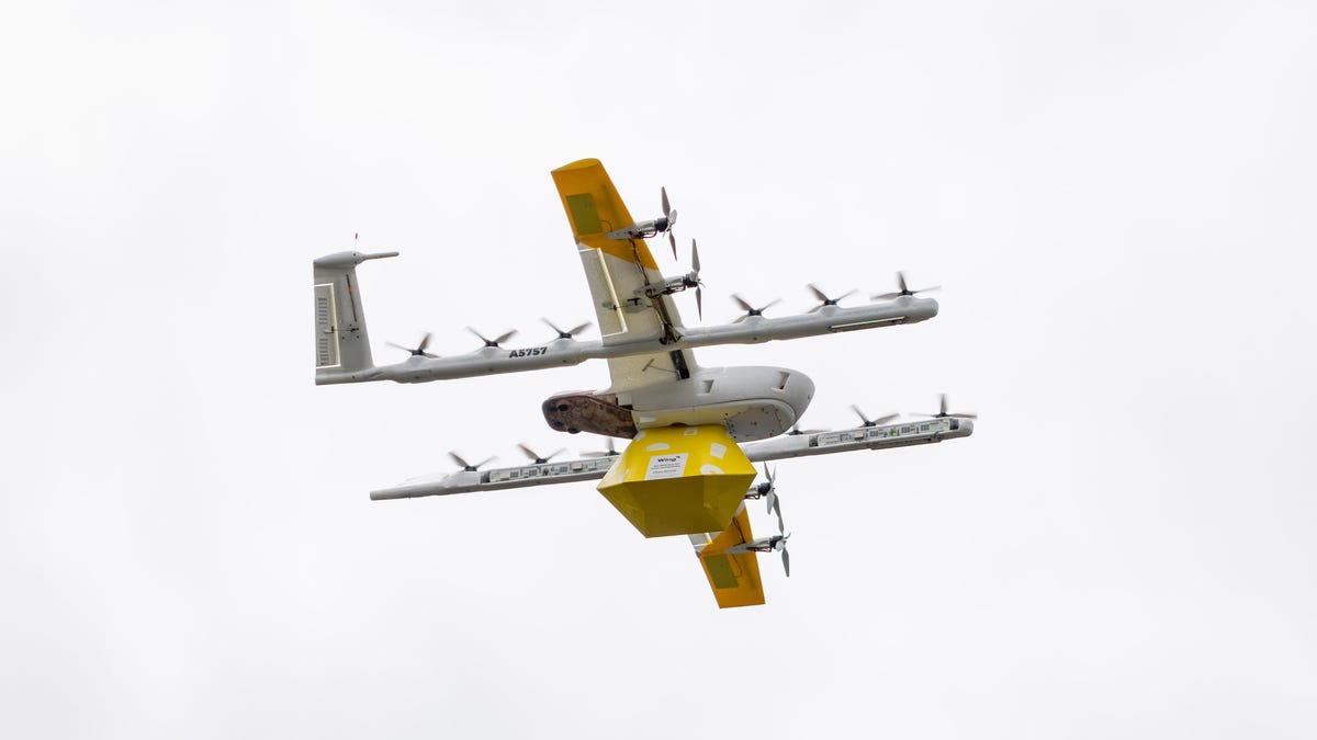A Wing drone with a recyclable waterproof box pulled up to the underside of the aircraft