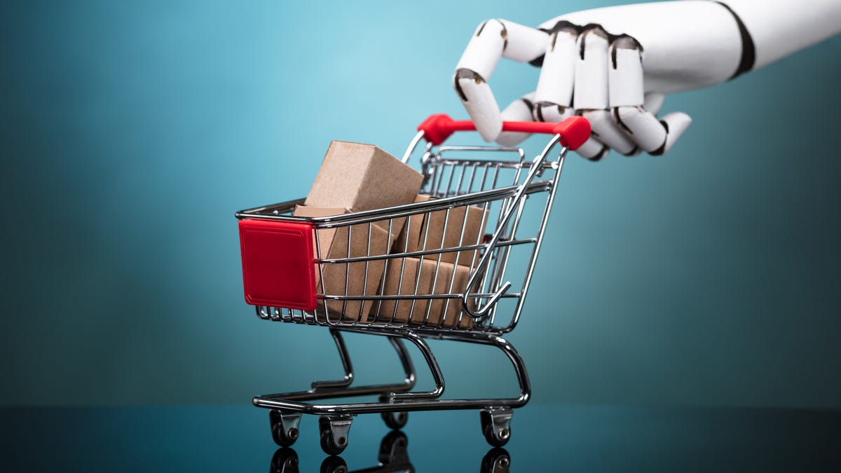 Photorealistic illustration shows a robot hand pushing a miniature shopping cart loaded with miniature parcels.