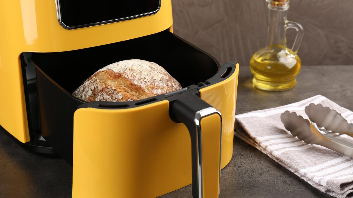 yellow air fryer with loaf of bread in basket and cruet of oil beside it