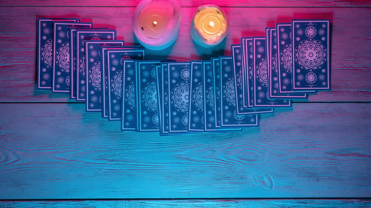 A photo of tarot cards on a table with two candles and a neon pink glow gettyimages-1276361910