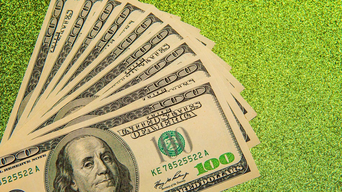 Several hundred dollar bills are laid out on a green background.