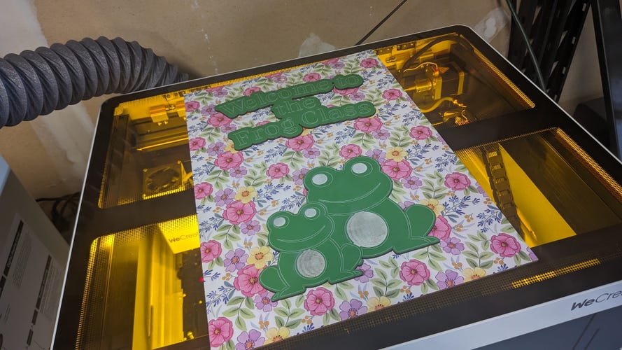 The WeCreat Laser with a laser cut frog on a flowery background