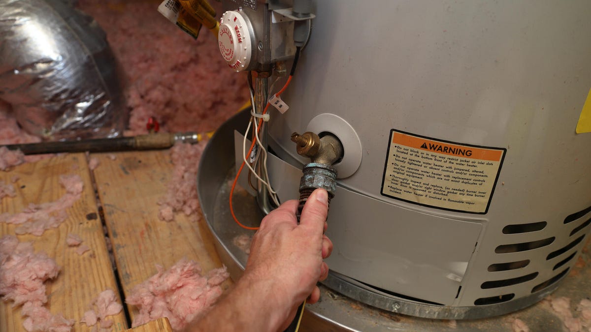 A hand turns the valve on a water heater.