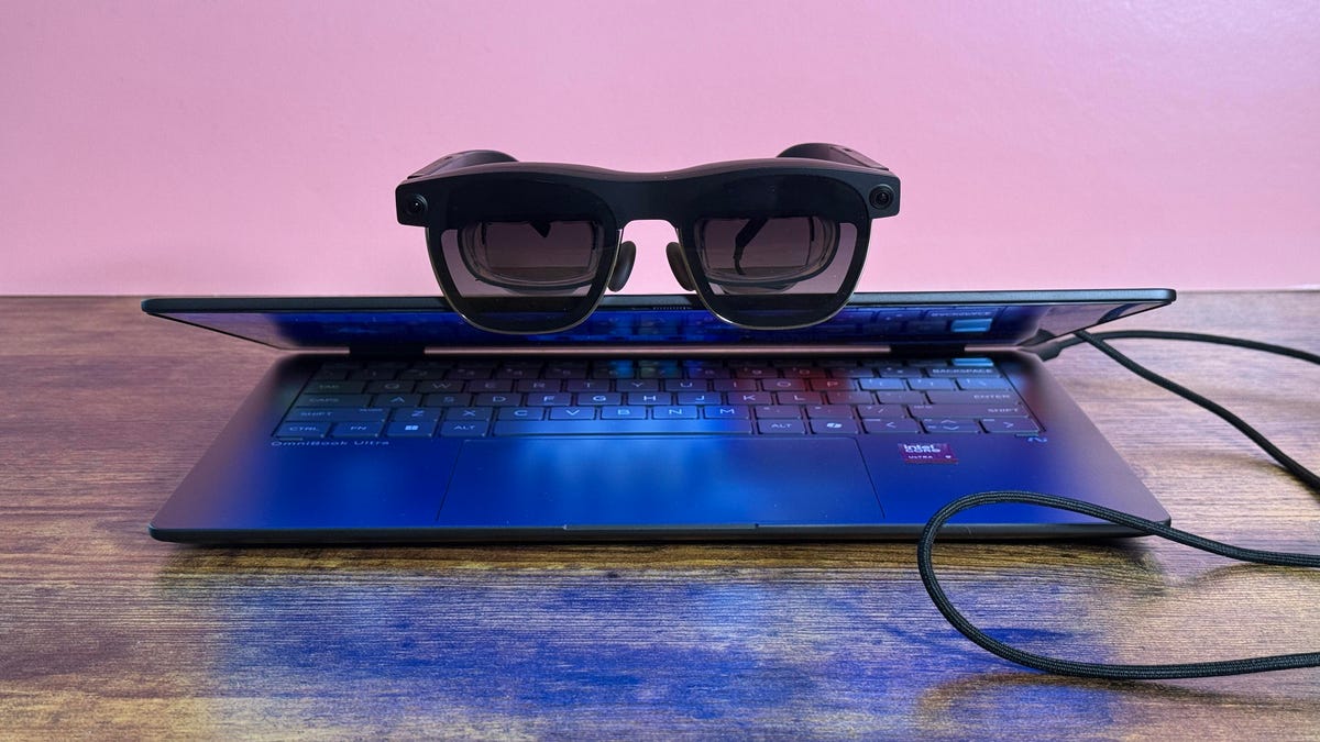 An open HP laptop with a pair of connected smart glasses perched on top