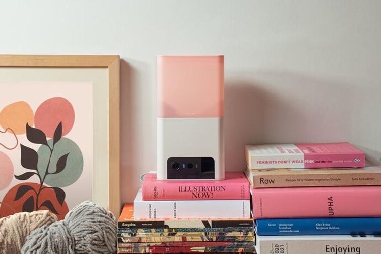 A Petcube Bites 2 Lite sits on top of books amid cozy decor.