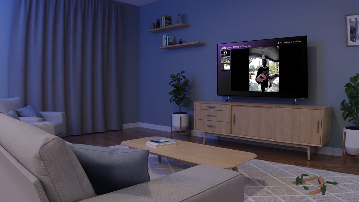 A living room Roku television displays the live feed from the home's video doorbell, where a delivery driver stands at the front door.