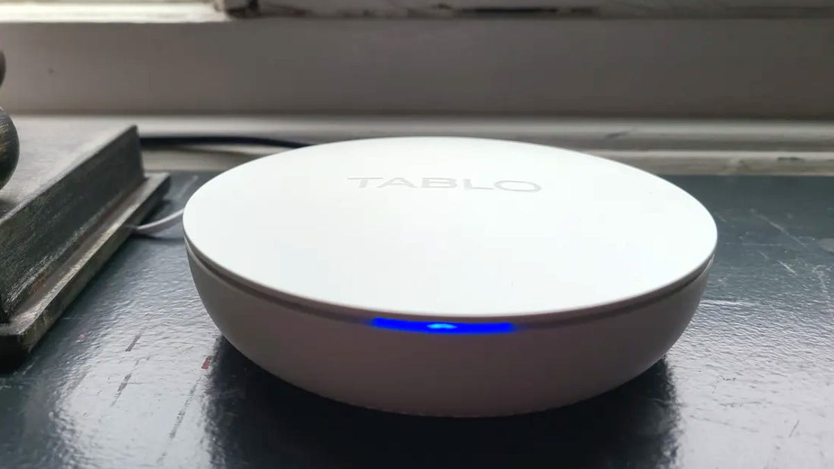 A white, disc-shape DVR with Tablo branding and a blue status light, set against a purple and blue background.