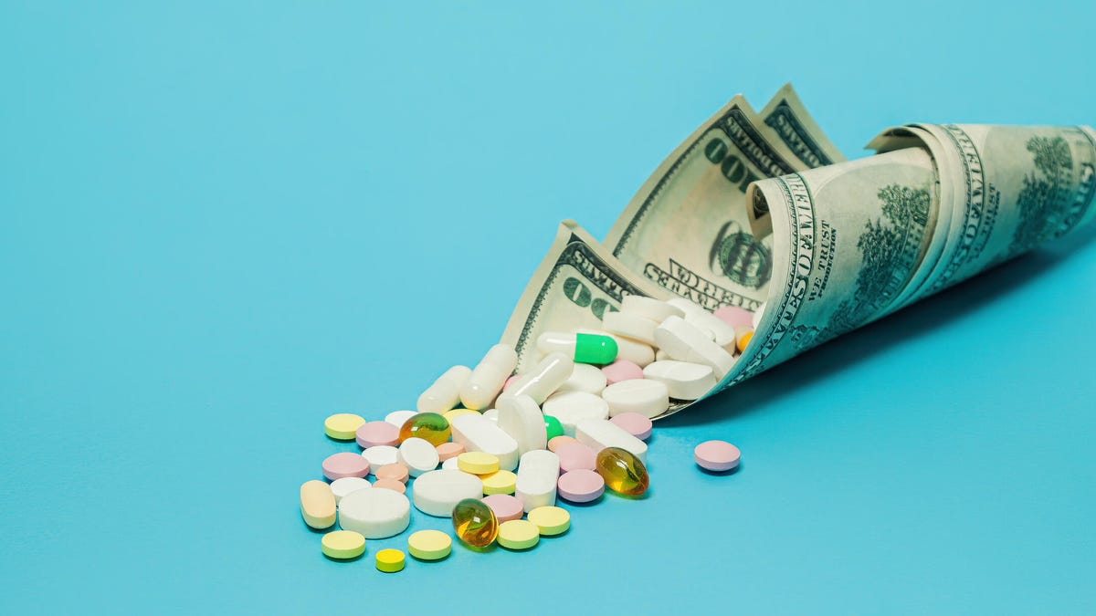 A handful of vitamin and supplements with money on a blue background.