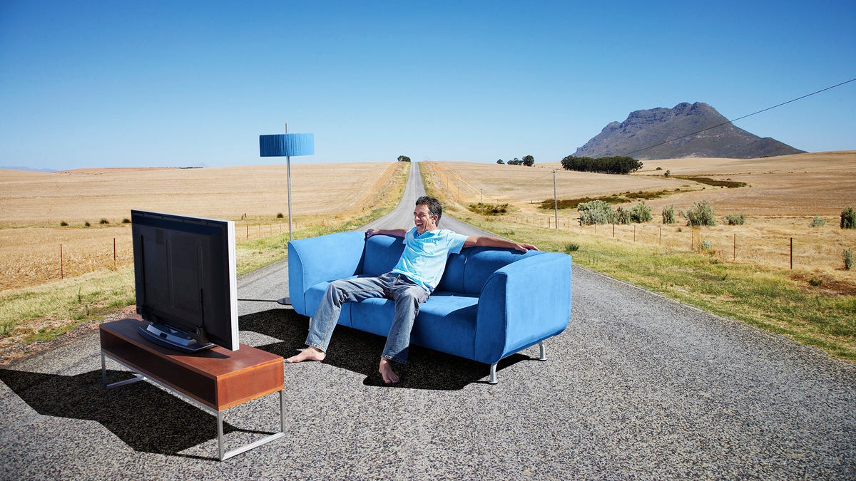 A person sitting on a small couch watching TV outside