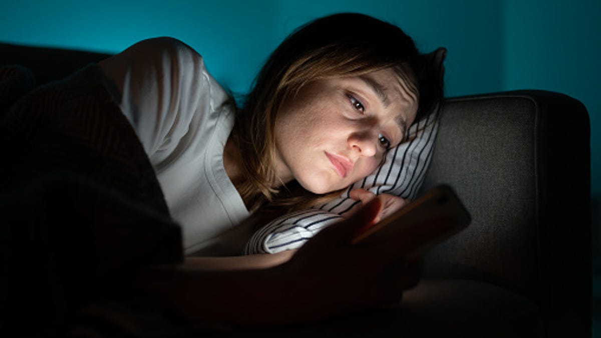 Woman lying in bed at night while scrolling through her phone.