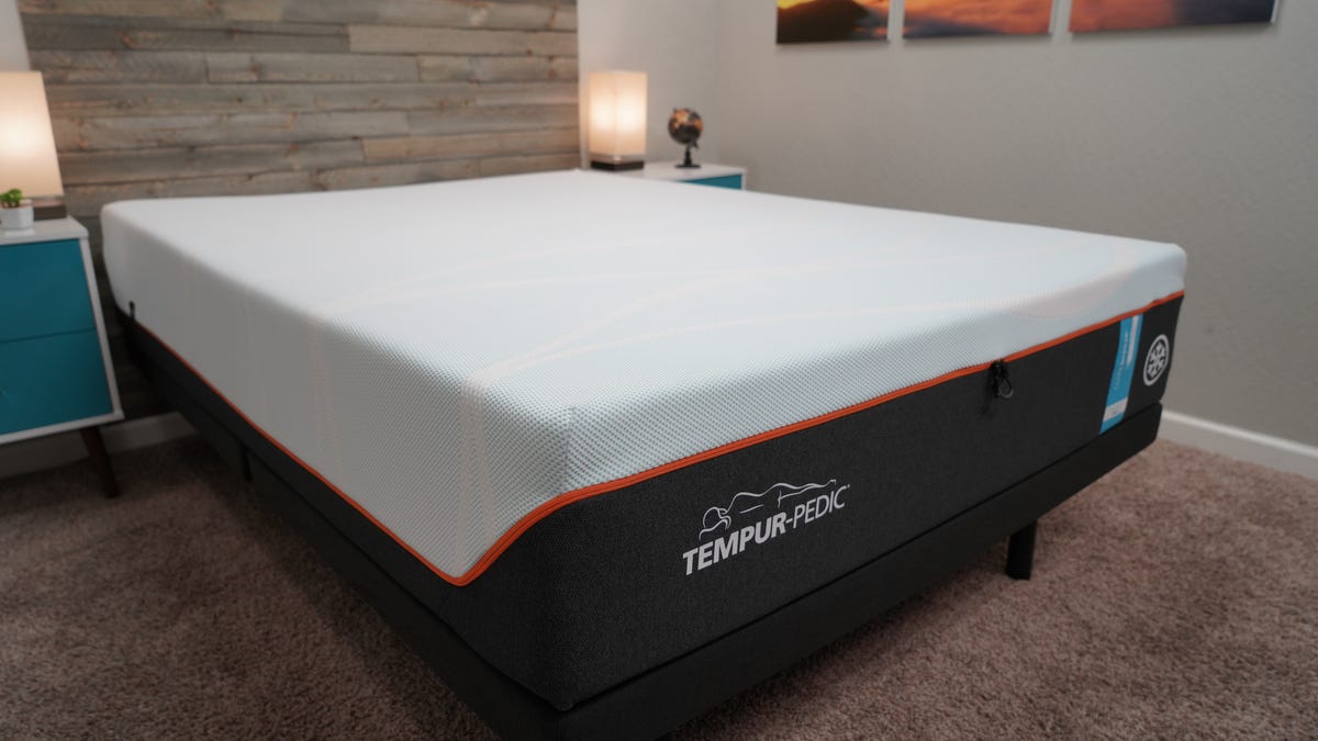 A Tempur-Pedic LuxeBreeze mattress sitting on top of a black bed frame inside of a well-lit room.