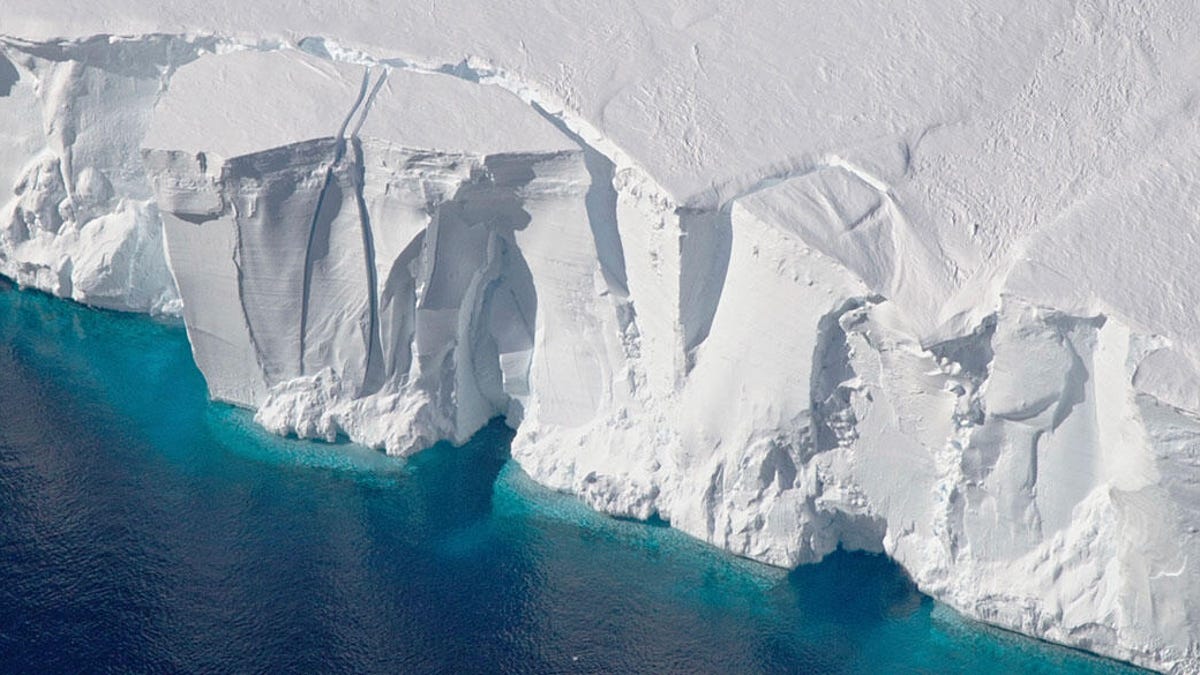 On the bottom left is a blue ocean, and the rest of the image is a pure white Antarctic ice shelf with a few cracks and jagged edges.