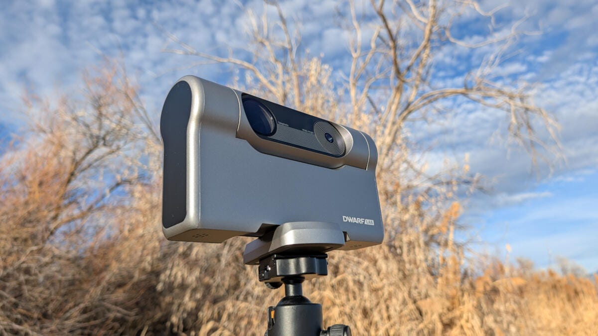 A smart telescope camera on a tripod with trees and a blue sky in the background