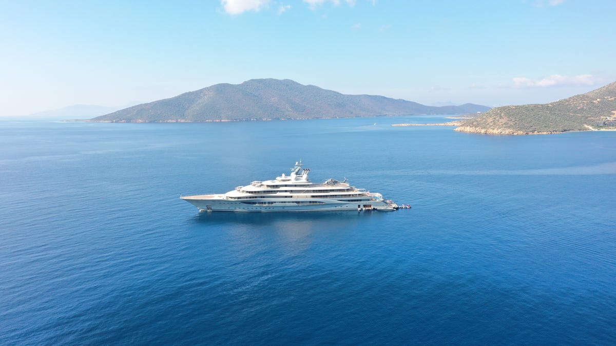 A large yacht in open water with a coastline in the background