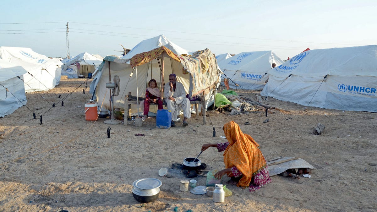 White tents with the United Nations seal represent makeshift camps for people displaced by Pakistan's floods. A woman is seen cooking on the ground, as her family waits in one of the tents.