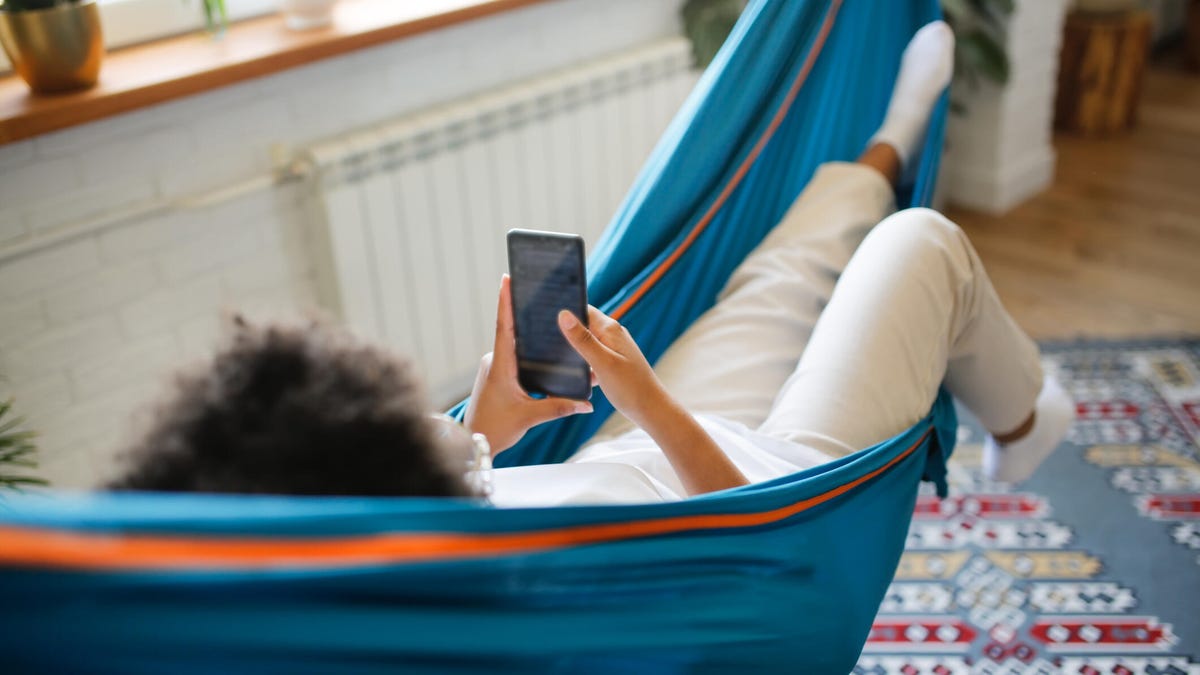 A person lounges in a hammock with a phone in their hands.