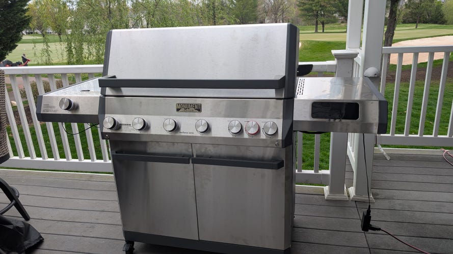 A large 6-burner grill on a deck with a golf course behind it