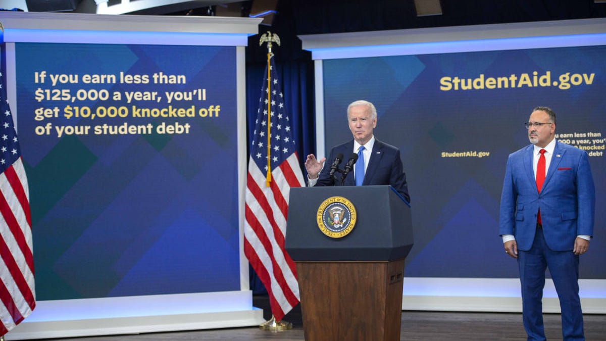 Biden stands at a lectern, in front of screens showing facts about the student loan forgiveness program.