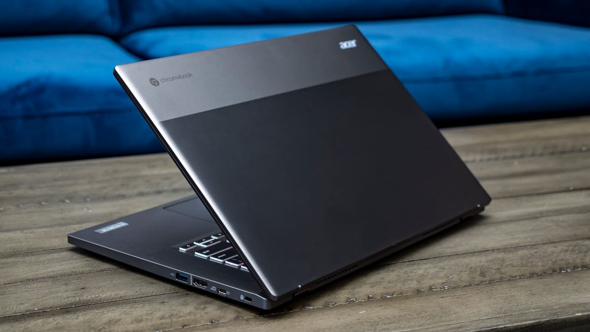 Acer Chromebook 526 GE laptop open facing away and to the left showing the two-tone gray lid and sitting on a wood table with a blue couch behind it.