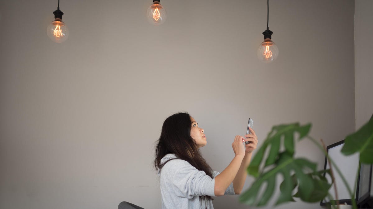 A woman uses her phone below three home lights.