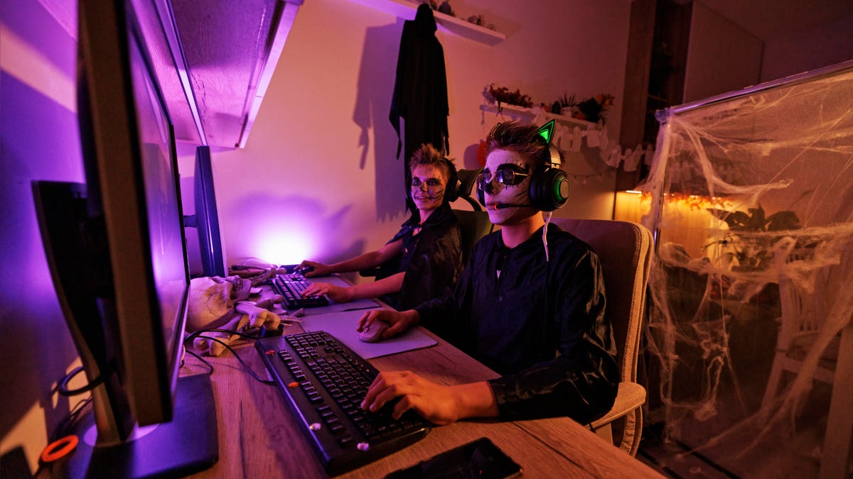 Two teenagers dressed for halloween playing video games on two computers
