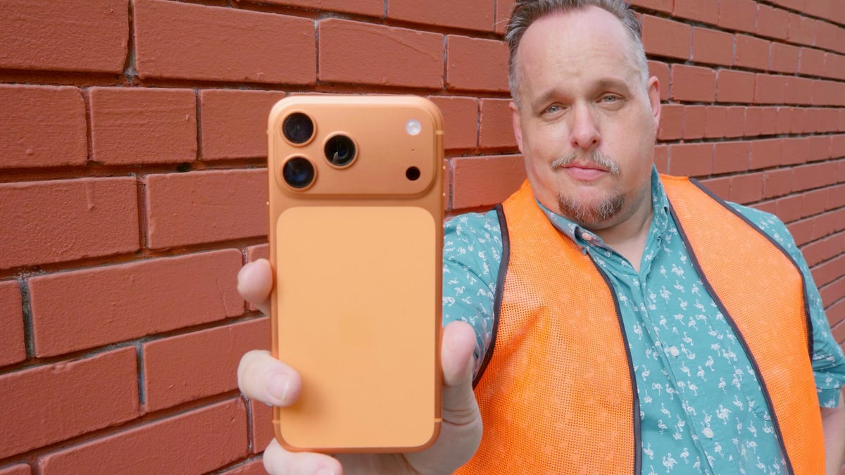 A man wearing an orange vest holding an iPhone 17 Pro Max in Cosmic Orange