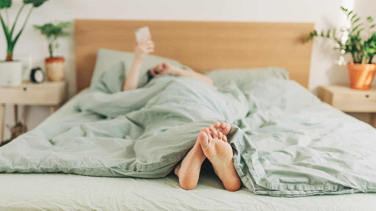 Person relaxing in bed with green bedding and sheets
