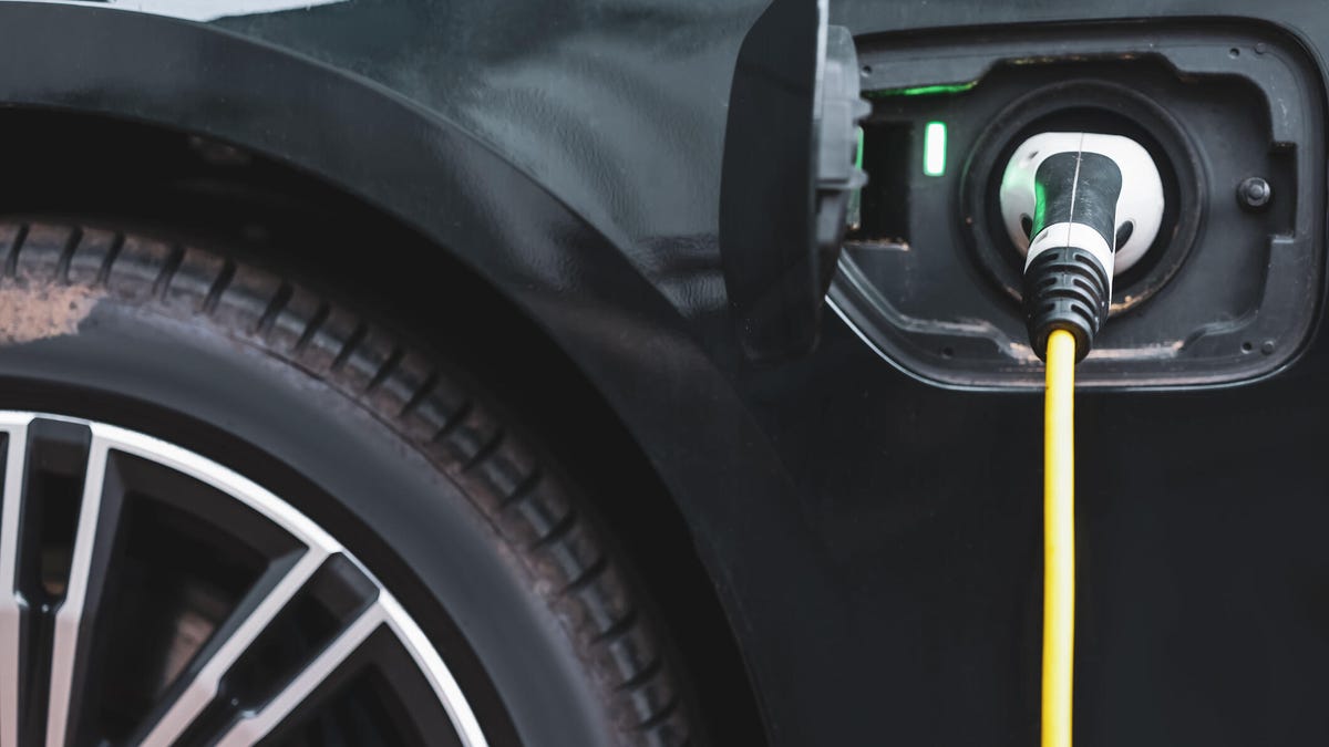 A black electric vehicle with a charger plugged into it, with a yellow cable running from the charger.