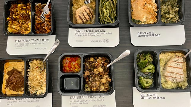 Six premade meals in plastic containers sitting on a desk