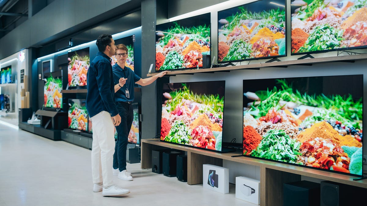 Two people looking at a wall of TVs