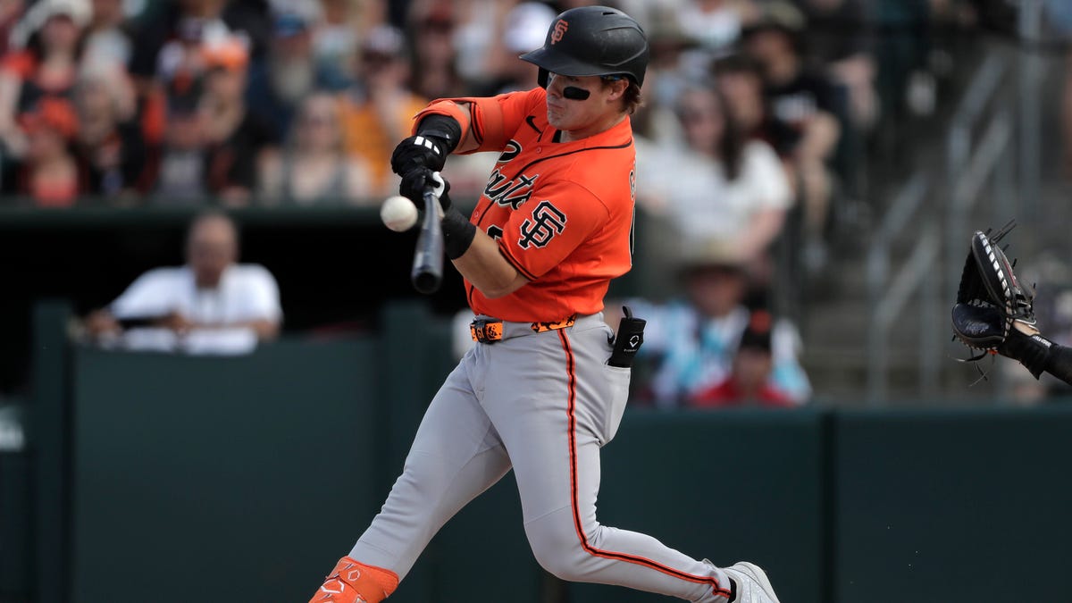 a left-handed hitting baseball player in an orange jersey with SF on the upper arm swing a bat just as the baseball arrives