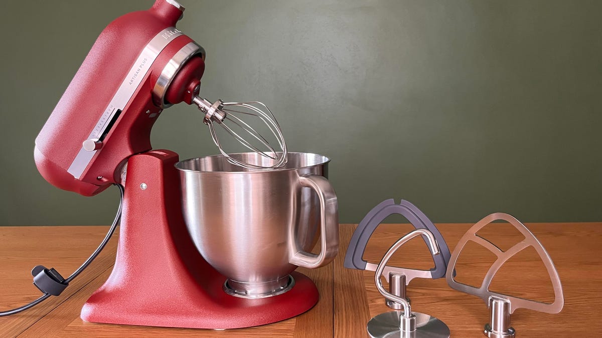 a red stand mixer on a wooden table with a green background