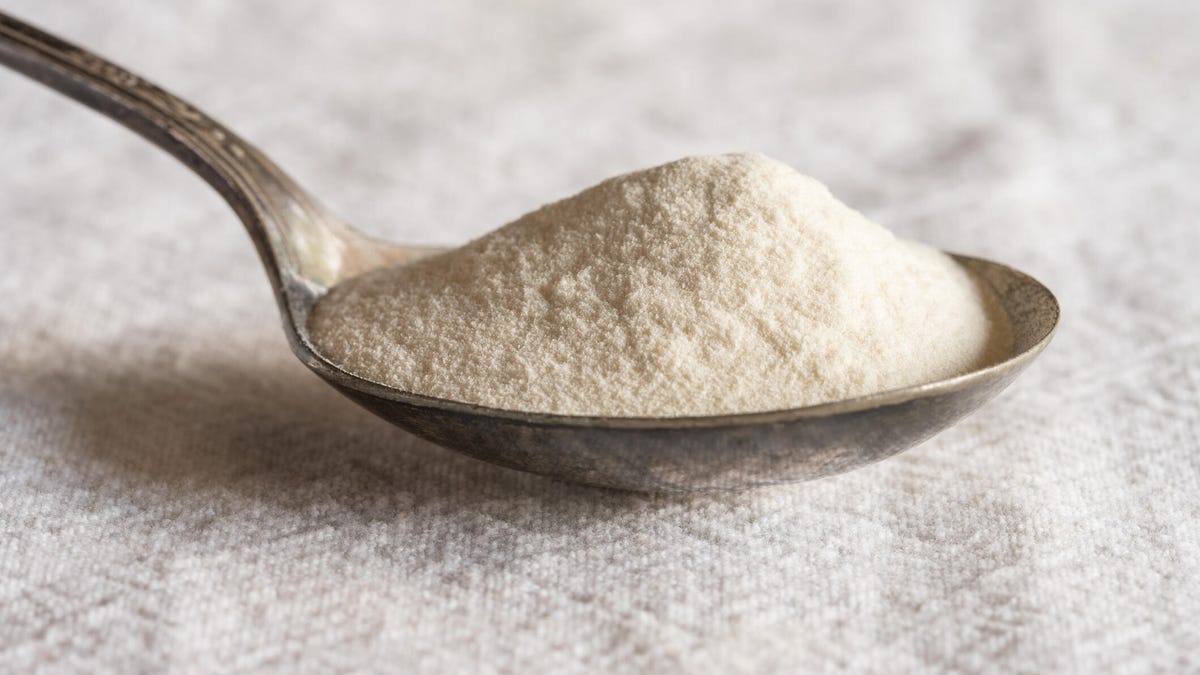 Xanthan gum powder on a spoon resting on a white textured surface.