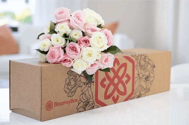 Photograph of pink and white floral bouquet sitting on top of a Bloomsybox delivery box on a countertop with blurred room in background