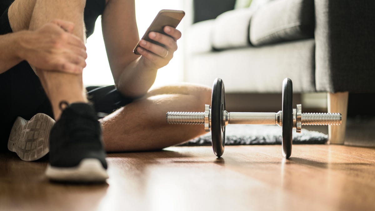 Man looking at phone with a dumbbell at home during workout