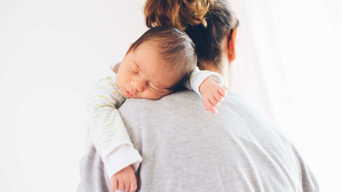 A tired woman holding her sleeping newborn close.