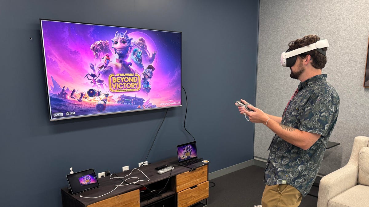 A man wearing a VR headset and holding controllers stands in front of a TV screen with the game's logo.