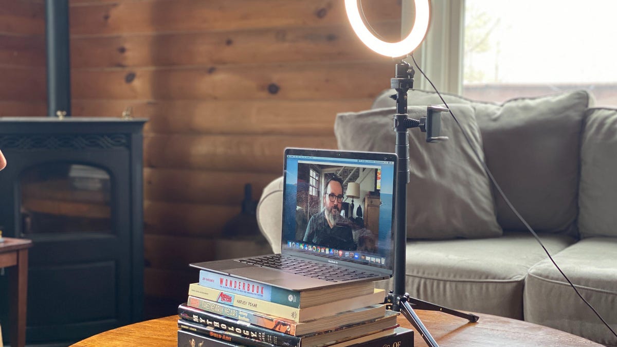 a MacBook on a pile of books with a ring light behind it