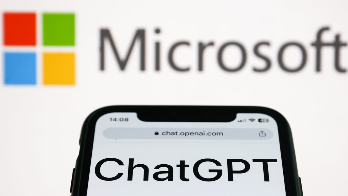 ChatGPT website displayed on a phone screen and Microsoft logo displayed on a screen in the background