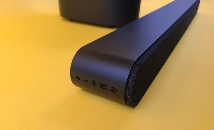 The side of a VizioSV210M Soundbar sits in front of a yellow background and shows volume, Bluetooth, menu and power buttons.