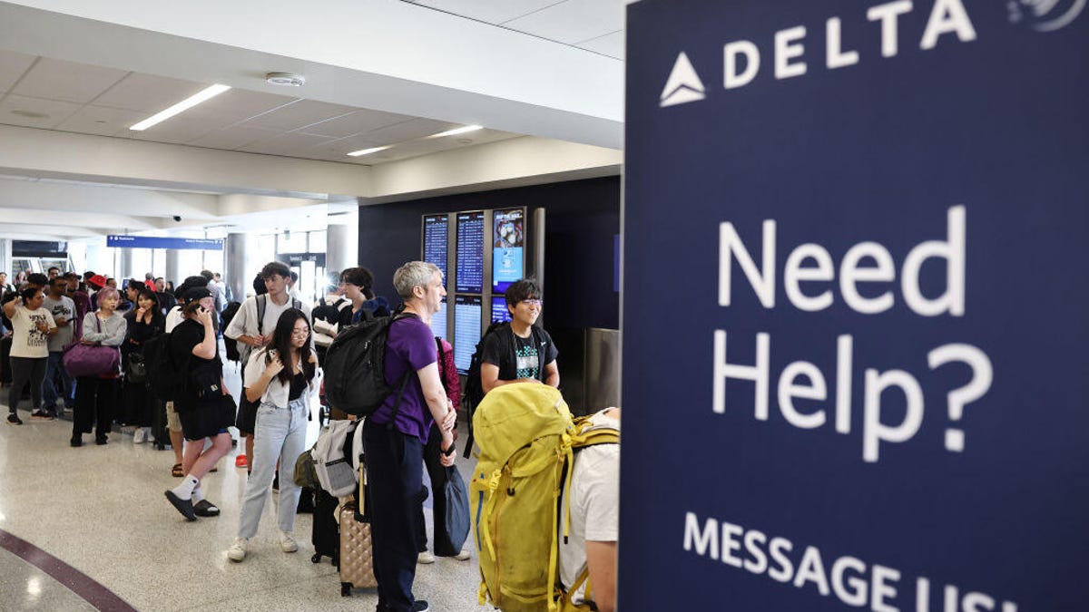 A group of airline travelers standing in front of a screen displaying flights.