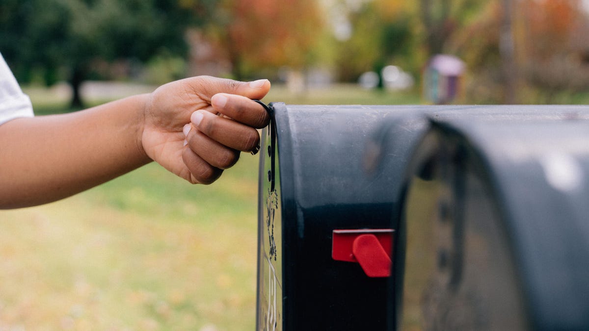 Close-up shot of a Black woman's hand opening a mailbox in the suburbs