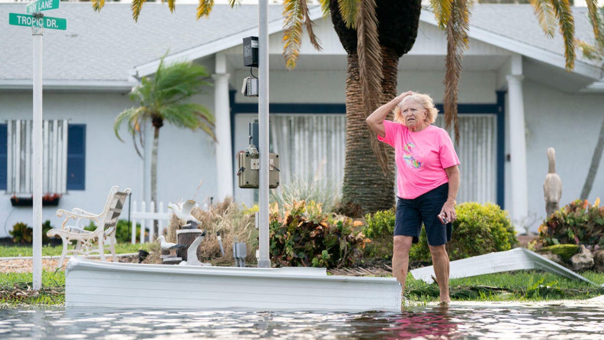 a woman walking down a flooded road after Hurricane Milton, a palm tree behind her