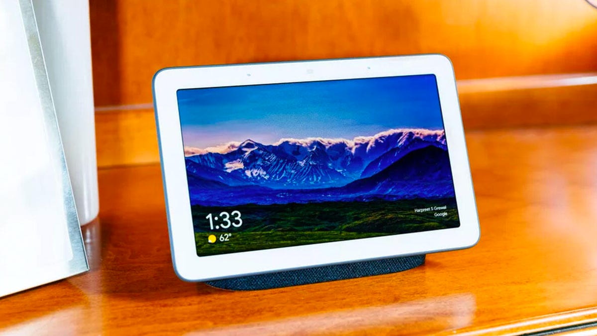 Google Nest Hub (2nd, gen) on a wooden surface with an image of mountains on the screen.