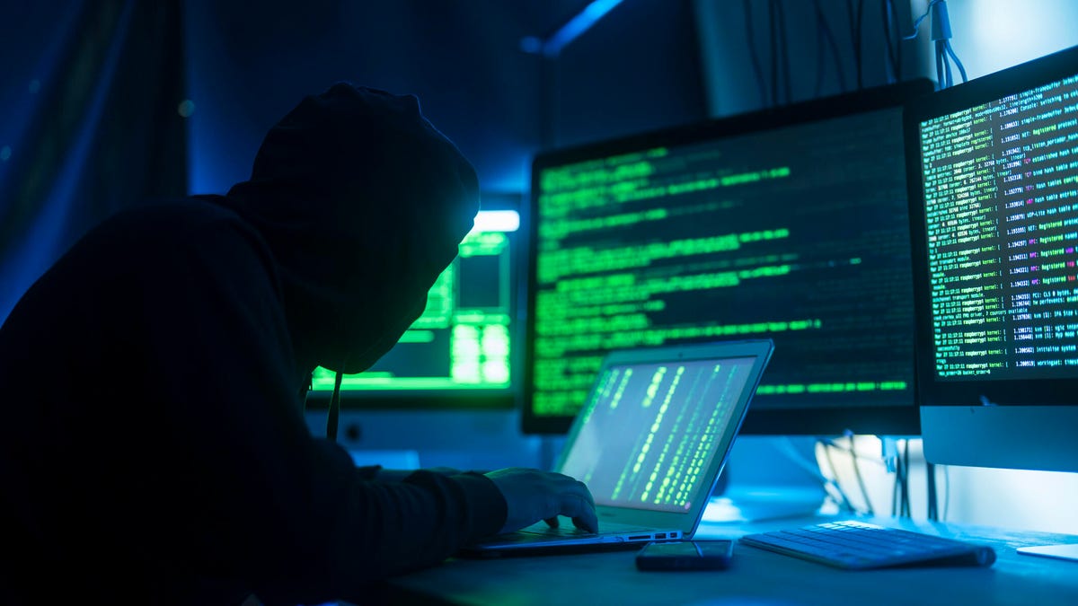 A silhouetted person in front of a laptop and several computer monitors